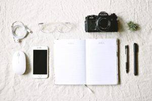 White Notebook Beside Pens and Gold Iphone 6 and Camera